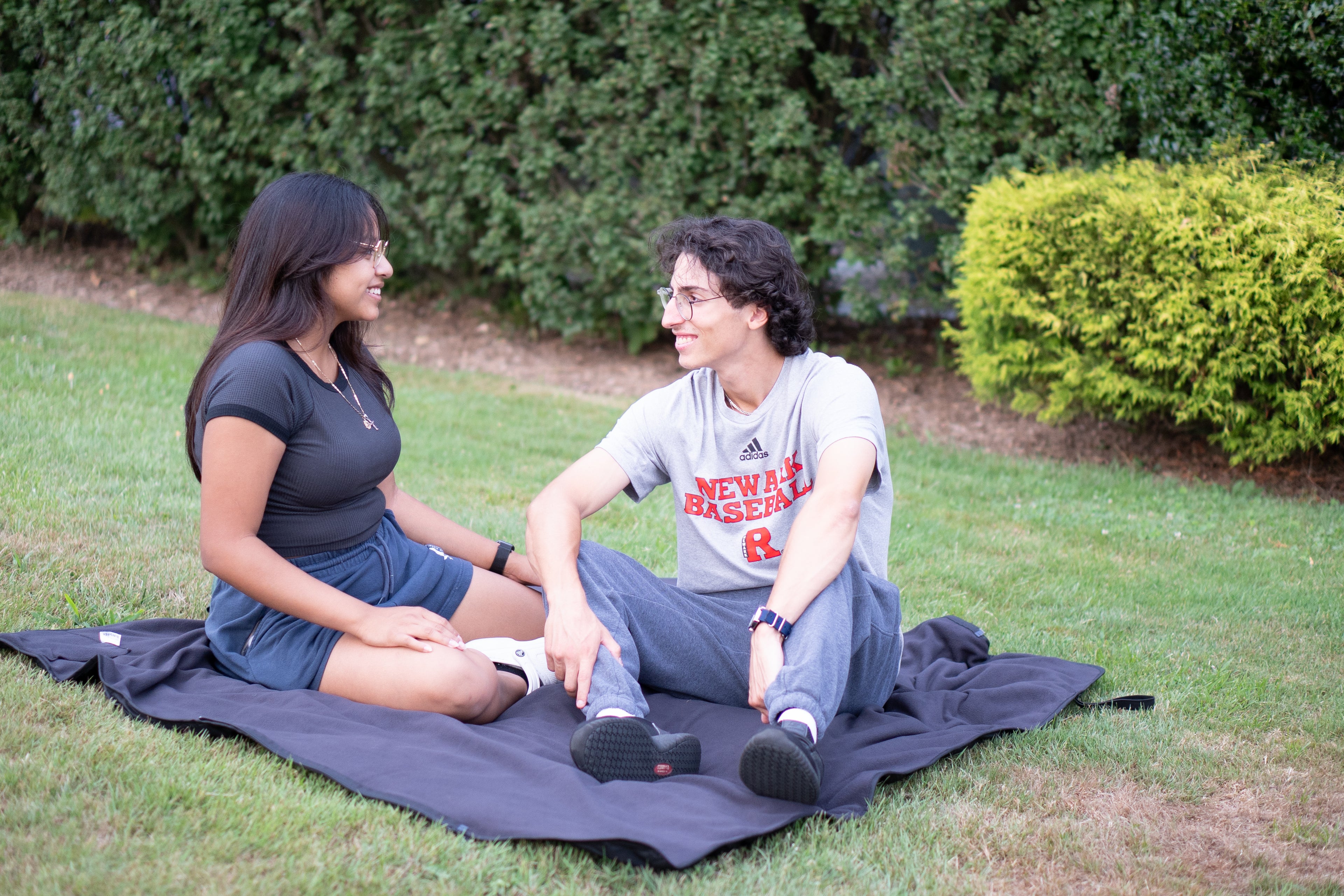 Couple smiling at each other sitting on the Ultimate SportsWrap as a blanket in a park.