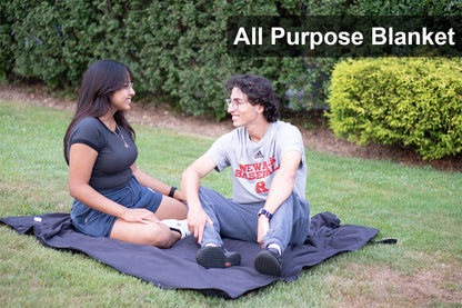 Couple smiling at each other and sitting in the park on the Ultimate SportsWrap using it as a blanket 