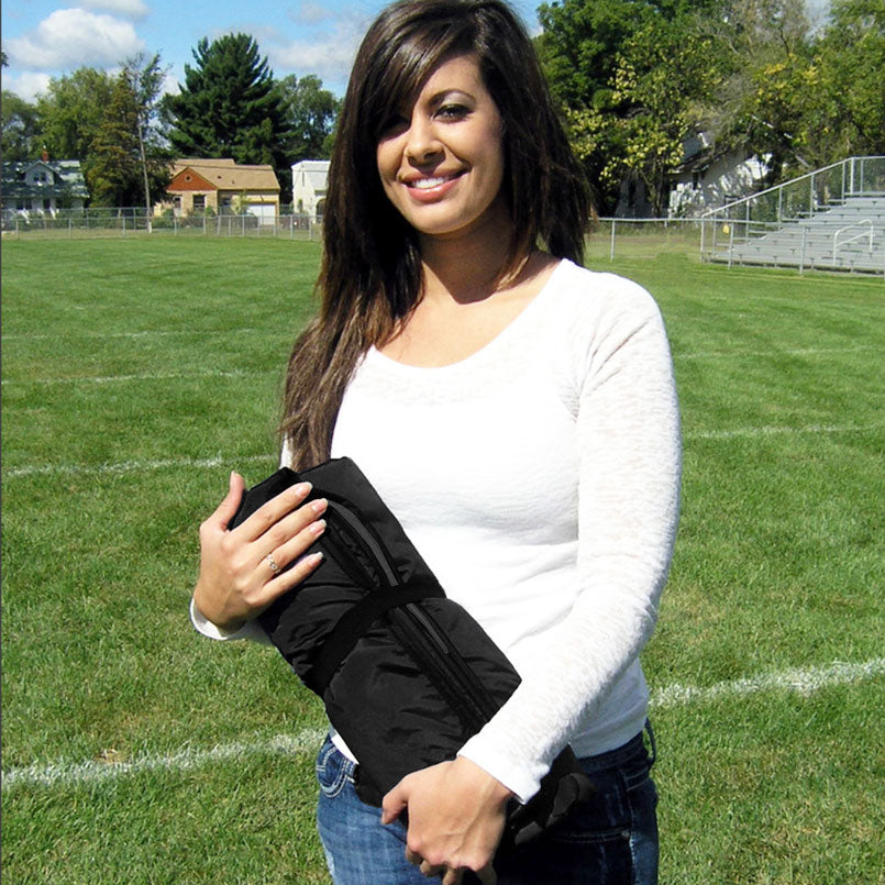 Woman standing on a grass field holding a rolled up black ultimate sportswrap